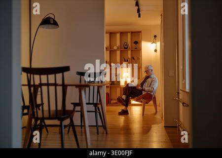 Senior Caucasian Man Sitting Alone in Living Room Reading and Relaxing Stock Photo