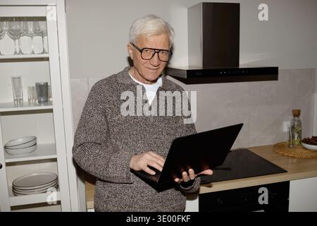 Portrait of Senior Caucasian Man Using Laptop Computer in Modern Kitchen Stock Photo