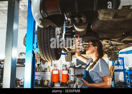 Young adult female mechanic inspecting car in auto repair shop Stock Photo