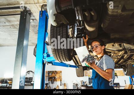 Professional female mechanic inspecting car in auto repair shop using digital tablet Stock Photo