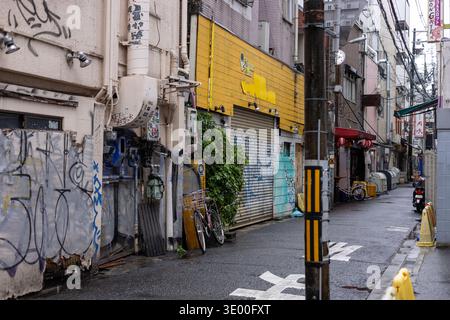 A gritty back alley with graffiti, closed shutters and bicycles in Namba, Osaka, Japan. Stock Photo