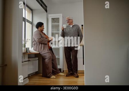 Senior Caucasian Man and Senior Black Woman Drinking Coffee and Smiling Indoors Stock Photo