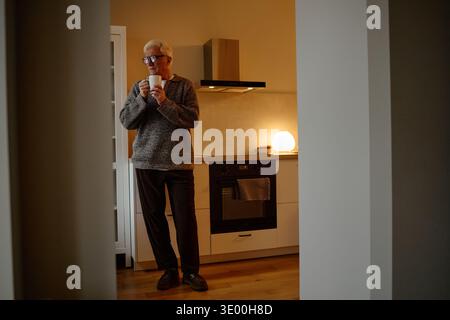 Senior Caucasian Man Drinking Coffee While Standing in Modern Kitchen Stock Photo