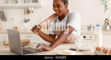 Woman Using Laptop While Baking in Kitchen During Daytime With Various Ingredients on Table Stock Photo