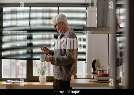Senior Caucasian Man Using Smartphone While Drinking Coffee Indoors Stock Photo