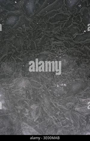Abstract background of dark natural ice surface with cracks and bubbles. Top view of frozen lake water with crystalline texture. Winter ice patterns o Stock Photo