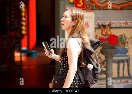 BANGKOK, THAILAND-FEB 15, 2026: Female tourist exploring temple, capturing cultural travel moments with smartphone, side profile Stock Photo