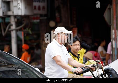 BANGKOK, THAILAND-FEB 15, 2026: Male tourist riding bicycle exploring market, casual urban walking Thailand, side profile Stock Photo