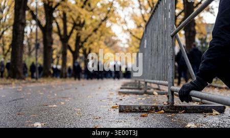 Close-up of a gloved hand gripping a metal crowd control barrier on a wet, leaf-strewn street. Stock Photo