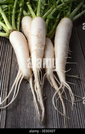 Whole daikon radish on rustic wood surface, white radish with greens, minimal food composition Stock Photo