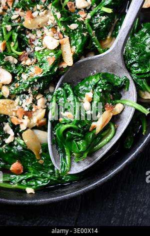 Top view of pan fried spinach with garlic and nuts on rustic wooden background. Healthy lunch idea, simple recipe and sustainable lifestyle concept Stock Photo