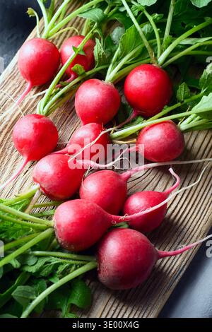 Red radish bunch with leafy tops on textured wooden cutting board. Natural produce for healthy recipes and rustic food photography Stock Photo
