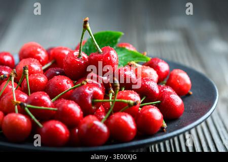 Cherries arranged on dark ceramic plate, rustic wooden background. Fresh organic red fruit, seasonal harvest Stock Photo