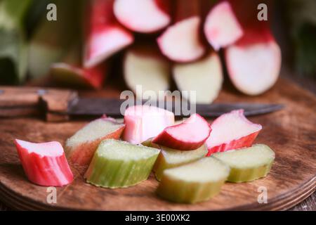 Close perspective of chopped rhubarb with kitchen knife on cutting board, rustic style. Organic rhubarb pieces detail, healthy seasonal cooking concept Stock Photo