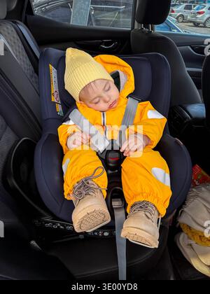 Sleeping baby in car seat wearing yellow winter snowsuit Stock Photo