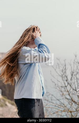 Woman Wind Hair Young woman with long brown hair stands outdoors on a breezy day wearing a blue shirt Stock Photo