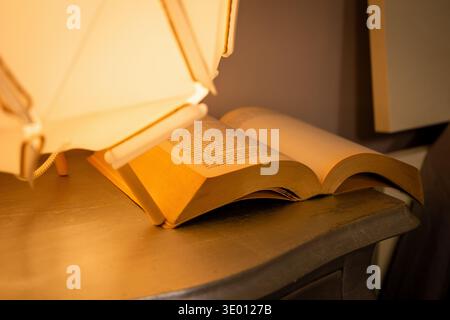 Warm bedside lamp creating cozy atmosphere in modern bedroom interior with books on nightstand. Stock Photo