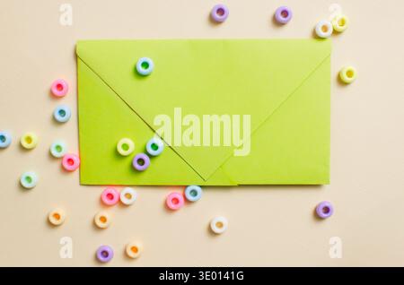 Bright green envelope on a light beige background decorated with multi-colored plastic beads in the shape of rings. A playful and creative composition Stock Photo