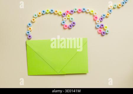 Bright green envelope on a light beige background with decorative pastel beads arranged in fancy lines. A playful and festive composition for a DIY or Stock Photo