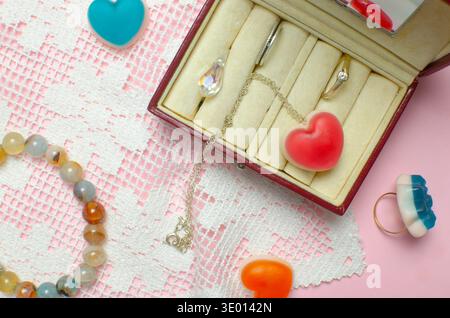 Jewelry box on pink background: rings, necklace with jelly red heart, crystal and colorful accessories. Jelly candies in the shape of hearts. Conceptu Stock Photo