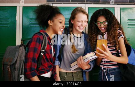 Gossip, smile or friends in high school with phone, conversation or bonding together in social media scroll. Happy, girls or students with chatting Stock Photo
