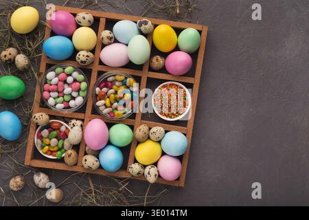 Colored easter eggs and small candies in frame on gray background Stock Photo