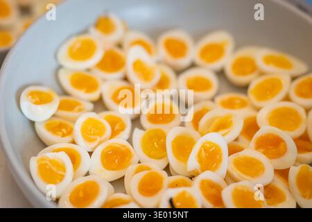 Halved soft-boiled quail eggs arranged in a white bowl, showing bright yellow yolks and delicate egg whites. Close-up of sliced quail eggs. Stock Photo