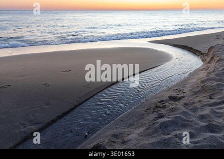 Small stream flowing across sandy beach into Mediterranean sea at sunset Alanya Turkey coast Stock Photo