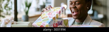Header of Young Black Woman Smiling While Opening Colorful Gift Box Indoors Stock Photo