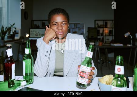 Young Adult Black Woman Sitting at Table Holding Beer Bottle Looking Unimpressed Stock Photo