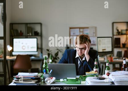 Young Caucasian Man Sitting at Desk Working Late Surrounded by Beer Bottles Stock Photo