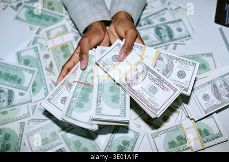 Caucasian Woman Holding Bundles of Us Dollar Bills over Table Covered with Money Stock Photo