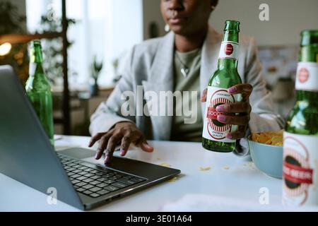 Young Adult Black Woman Using Laptop While Drinking Beer Indoors Stock Photo