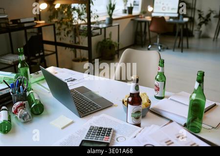 Messy Office Desk Featuring Laptop and Beer Bottles during Workday Stock Photo