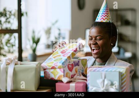 Young Adult Black Woman Smiling While Opening Birthday Gift Boxes Indoors Stock Photo