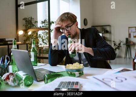 Young Caucasian Man Drinking Beer While Working at Office Desk Looking Stressed Stock Photo