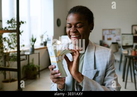 Young Adult Black Woman Smiling While Holding Stack of Money Indoors Stock Photo