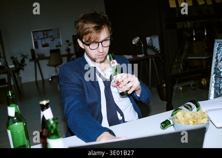 Young Caucasian Man Drinking Beer While Working Late Night in Office Stock Photo