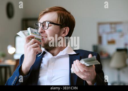 Caucasian Young Adult Man Smiling While Holding and Smelling Dollar Banknotes Stock Photo