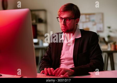 Young Caucasian Man Wearing Glasses Working on Computer in Office at Night Stock Photo