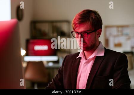Young Caucasian Man Wearing Glasses Working on Computer in Office Setting Stock Photo