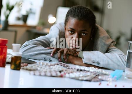 Portrait of Young Adult Black Woman Contemplating Medication at Desk Stock Photo