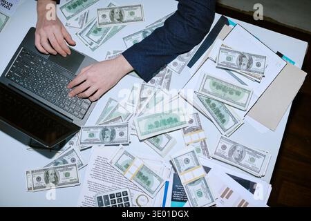 Caucasian Young Adult Man Using Laptop Surrounded by Stacks of Dollar Bills Stock Photo