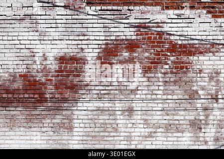 Aged red brick wall with distressed, peeling white paint and weathered texture. Authentic vintage masonry in Menomonie, Wisconsin, USA. Stock Photo