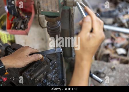 Focused worker hand drilling hole into metal part using machine. This industrial manufacturing process inside workshop requires skill and precision Stock Photo