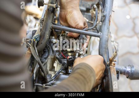 Focused mechanic with dirty hands at work on motorcycle engine repair. This detailed view shows professional labor, service, and maintenance in garage Stock Photo