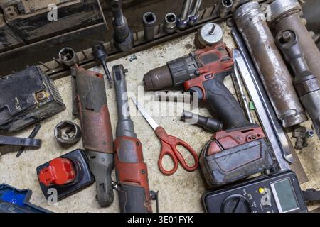 Overhead view of mechanic tool equipment on workbench in busy workshop. Power tool, cordless drill, and various repair instruments create cluttered sc Stock Photo