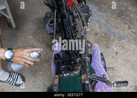 Focused man doing motorcycle repair, using spray can to paint metal frame. This DIY restoration and maintenance project in garage shows deep concentra Stock Photo