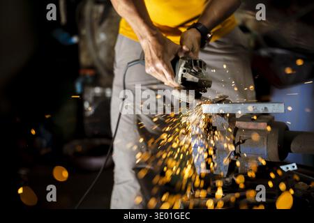 Focused craftsman working in workshop, using an angle grinder on metal. Bright hot sparks fly from cutting process, showing intense manual labor and s Stock Photo