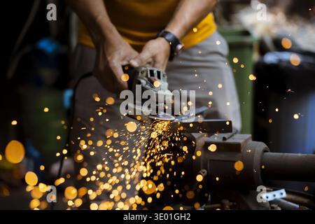 Focused man at work in workshop using power tool. industrial worker grinds metal with an angle grinder, creating shower of bright hot sparks from fric Stock Photo